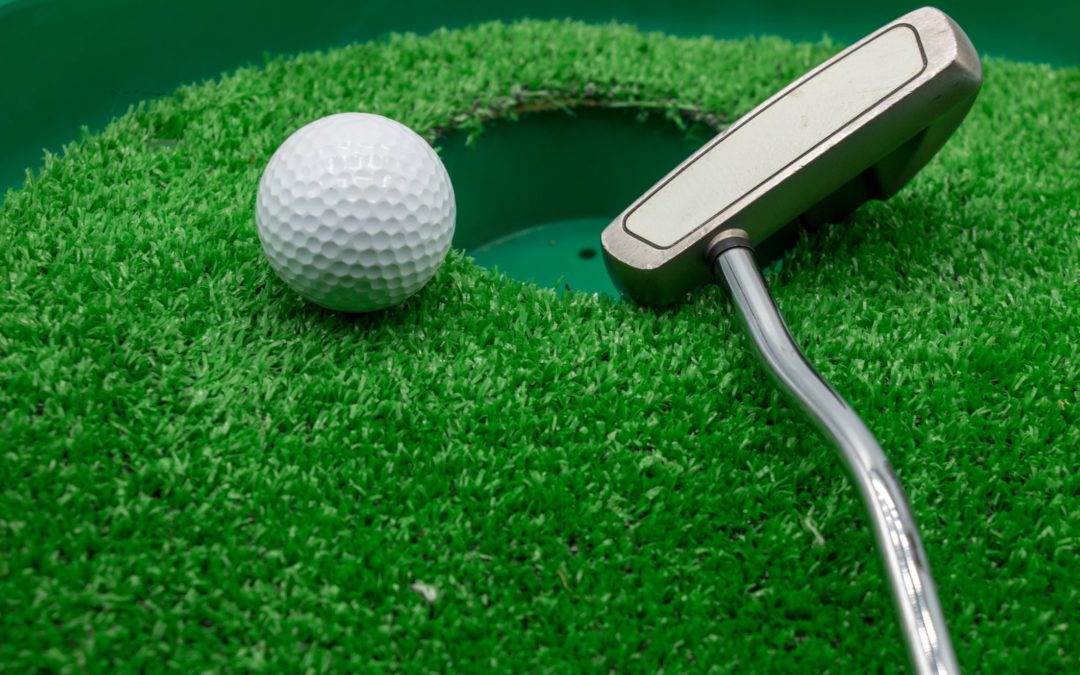 Golf ball and putter resting near a hole on an indoor putting green.