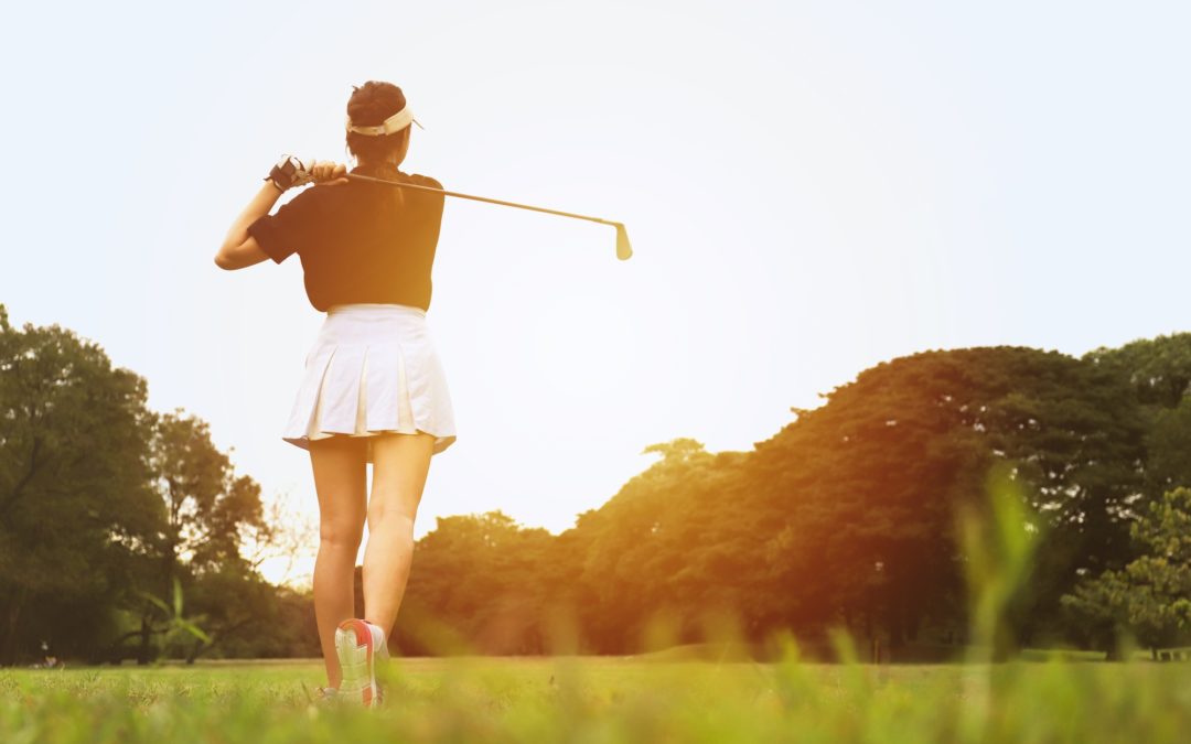 Woman golfing during late afternoon on golf course with trees.